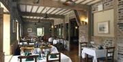 A stone dining room with wooden beams crossing the ceiling and tables set.