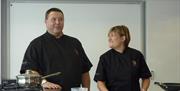 Two cookery teachers teaching a lesson with kitchen equipment.