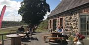 Stone cottage with people dining outside at picnic tables.