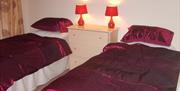 A bedroom with two single beds, a chest of drawers and two red lamps.