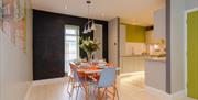 An open plan dining room and kitchen area with an orange and grey dining table and chairs.