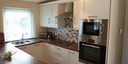 A kitchen area with an oven/microwave, hob, sink and a window.