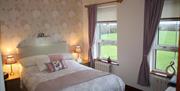 A double bedroom with wallpaper, bedside tables and two windows.