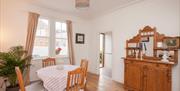 A dining room with a table and chairs, cupboard, a window and a potted plant.