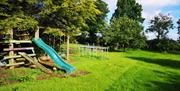 A garden with trees and a wooden playset with swings and a slide.