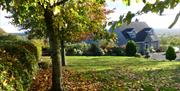 A lawn with falling leaves of a large grey house in the hills.