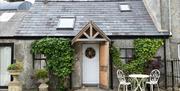 Outside view of Milk House with greenery on the walls and outside table and 2 chairs