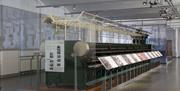 A large old spinning frame exhibit behind glass with information displays.