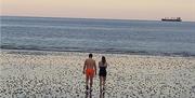 A couple in swimming costumes walking down the beach towards the water for cold water dip