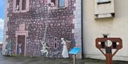 Medieval wall mural in Carrickfergus, with stocks beside it.