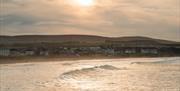 Soft sunlight reflecting off gentle waves with a  Castlerock town and rolling hills in the background under a cloudy sky