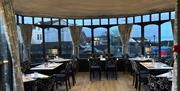 The conservatory area in The Stables Groomsport. View through set tables with sea view beyond.