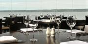 Waterfront restaurant with many tables set with wine glasses, cutlery and salt and pepper shakers.