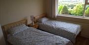 Image shows twin bedroom with beside table and lamp between beds