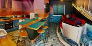 A photo of a kitchen and living area with ocean-themed murals, a boat-shaped couch, a kitchen island with bar stools, and a mural of the Titanic on th