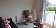 Living room with an arm chair, coffee table and patio doors out to the garden