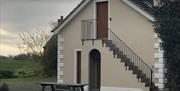 Image shows outside staircase to upstairs door of property. Also, wooden seating bench on ground outside side door of property