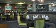 Photo of the Green Room restaurant inside the Crowne Plaza Belfast hotel. Semi-circle booth with set table at the foreground, other set tables and rai