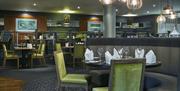 Photo of the Green Room restaurant inside the Crowne Plaza Belfast hotel. Semi-circle booth with set table at the foreground, other set tables and rai