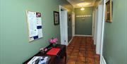 Image shows tiled hallway and table with visitor book and tourism book. Notice board above table with information on