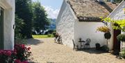 An outside area of the cottage with seating areas, flowers, a decorative bicycle and a view of the lough.