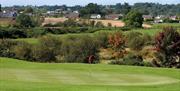 Image shows golf course with houses and countryside in the background