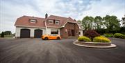 Image shows front of property with orange coloured super car in the large driveway