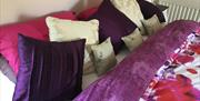 A large purple double bed with lots of cushions.