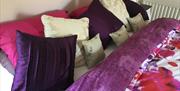 A large purple double bed with lots of cushions.