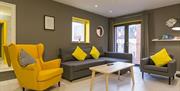 A grey sitting room with grey and yellow chairs, a grey sofa and a coffee table.