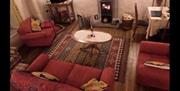 Living room with a red suite, carpet, coffee table, TV, woodburning fireplace and a table & chairs.