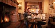 Couple sitting in front of open fire enjoying a meal and toasting their wine.