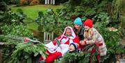 Three children are laughing and sitting with Santa in his sleigh on the grounds of Hillsborough Castle and Gardens. Santa is in a red suit.