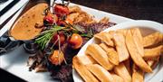 An image showing a plate of steak and chips with pepper sauce and tomatoes.