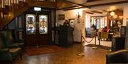 The lobby area features stained glass double doors, a wooden staircase, a reception desk, and armchairs for lounging.