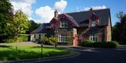 Rossclare Lodge front view of the house. A large lawn area in front of a large house in Donegal stone and a smaller painted extension to the left. A d