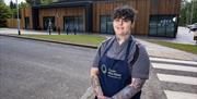 Chef Lauren Shimmon, Tailors House, Ballygawley, wearing her grey chef clothes and navy branded Mid Ulster apron standing in front of the new Pomeroy