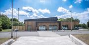 Image of the new visitor centre at Pomeroy Forest.  Exterior wooden cladding with large square windows to the ground and a mixture of flat and slanted