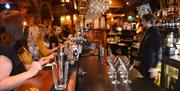 A hen party group of women seated at the bar in Jack's Bar, watching a bartender prepare drinks for a cocktail class. The bar counter is lined with co