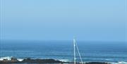 Blue sky and sea in the background, white sailing boat in the foreground with wooden fence atop stone wall left to right at the front