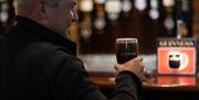 Gentleman drinking a freshly poured pint of Guinness in a branded glass at the bar of Charlie's Bar Enniskillen