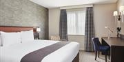 Photo of a double bedroom in the Holiday Inn Belfast City Centre. There is a king size bed on the left, desk on the right against the wall and a chair