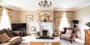 Image shows large lounge area with sofa, armchair, fireplace and TV