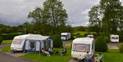 People sitting outside their caravans on their lots with a dog.