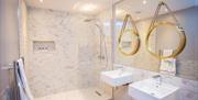 A photo of a bathroom with a large mirror, walk in shower and two sinks with their own mirrors.