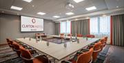 A large meeting room with a projector, screen and a large U-shaped conference desk.