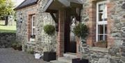 Image shows outside of stone property with bay tree plants at either side of front door