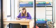 A photo of a traveler sitting at a desk in front of a bunk bed in a hostel.