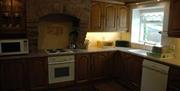 A stone kitchen with a microwave, hob/oven, dishwasher and a window.