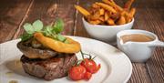 Steak served with onion rings and tomato on white crockery with side of chips and pepper sauce